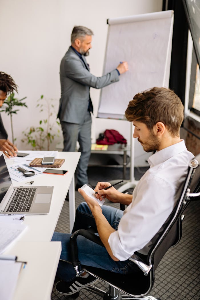 Business professionals engaged in a collaborative meeting, taking notes and discussing ideas on a flipchart.